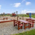 Spielplatz mit Sandkasten, Schaukel und Tischbank auf Kiesfläche.