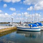 Boote liegen im Hafen, ein rotes Haus ist im Hintergrund sichtbar.
