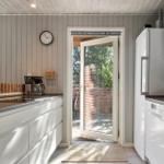 Küche mit weißer Einbauküche, Kühlschrank und Tür zum Garten.