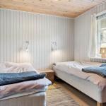 Zwei Betten mit Bettwäsche und Decken. Holzwand und Fenster mit Vorhang.