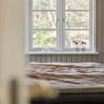 Ein Bett vor einem Fenster mit Waldblick und Blumenvasen.