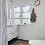 Badezimmer mit Waschbecken, Fenster, Uhr und Toilette.