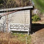 Weißer Holzstuhl vor einem grauen Holzhaus in einer grünen Umgebung.