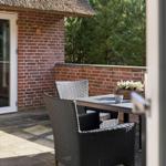 Terrasse mit Tisch und Stühlen vor einem Haus mit Strohdach und Backsteinmauer.