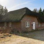 Ein Haus mit Strohdach und Backsteinfassade, umgeben von Bäumen und einem Kiesweg.