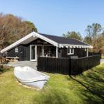 Black wooden house with terrace and white boat on grass.