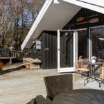 Deck with table, chairs, and grill. Black siding and white roof structure.