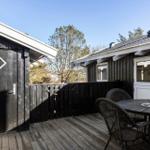 Deck with table and chairs in front of two wooden houses with white doors and roofs.