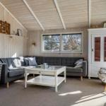 Living room with gray sofa, white table, and wood walls. Windows and cabinet are visible.