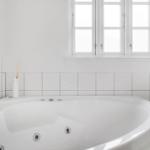 A white bathtub with whirlpool under a window with white frames.