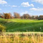 Golf course with green turf, trees, and blue sky with clouds.