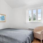Bedroom with bed, chair, and window. Wall art and wooden floor.