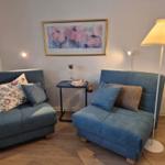 Two blue seating units with cushions, table, and floor lamp in a room with wooden floor.