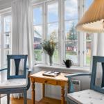Two blue chairs and a wooden table are by a window overlooking the street.