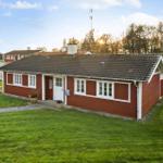Red wooden house with white window frames and roof, surrounded by grass and trees.