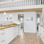 Modern kitchen with wooden countertop and white cabinets. Upper level with wooden railing.