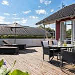 Terrace with table, chairs, loungers, and umbrella. Background: house and hedge.