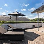 Terrace with lounge chairs, umbrella, and hammock. Wooden deck and green hedge in the background.