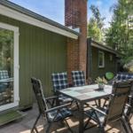 Terrace with table and chairs in front of green house with chimney.