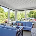 Patio with blue sofa and armchairs, large windows overlooking green trees.
