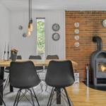Dining area with wooden table, black chairs, and wood stove against brick wall.