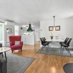Living and dining area with wooden floor, white wall paneling, and a wood stove.