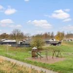 Green playground with slide and swing in front of modern houses on a lawn.