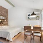 Bedroom with bed, table, and chairs. Wooden wall, white walls and ceiling.