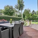 Deck with table and chairs, surrounded by green hedges and trees.
