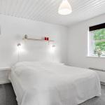 Bedroom with white bed, window, and wooden shelf.