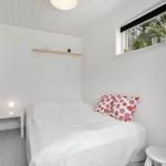 Bedroom with white bed, red cabinet, and window with view of trees.
