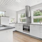 Modern kitchen with white cabinets, stainless steel appliances, and large windows overlooking greenery.
