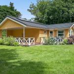 Yellow vacation home with balcony and green lawn. Surrounded by trees and shrubs.