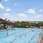 Outdoor pool with swimmers and view of water and trees.