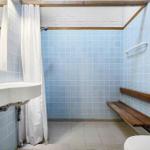 Bathroom with blue tiles, sink, shower, and wooden bench.