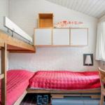 Room with double bed, daybed, and wooden shelves against white brick wall.