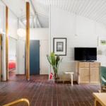 Living room with TV, plant, and seating. Wooden floor and white walls.