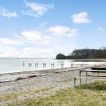 A picnic table stands by the shore next to a lake. Trees and a clear sky are visible in the background.