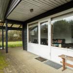 House with large window, terrace, and garden. View into living room with sofa.