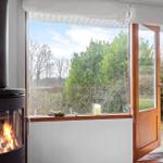 A wood stove stands before a large window with a view of a garden.