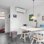 Dining area with white table and chairs, wall clock, and artwork. Passage to the toilet.