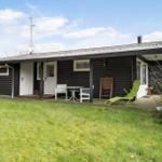 A black wooden house with a terrace, green lounge chair, and white table.