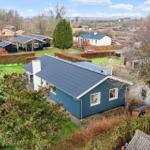 A blue house with a dark roof and garden in the background.