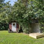 Red wooden shed with white door in garden under trees.