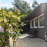 Wooden terrace with seating area in front of a dark gray house with windows.