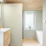 Bathroom with sink, mirror, and bathtub. Wooden ceiling and window with plant.