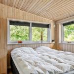Bedroom with wooden walls, large bed, and windows with view of trees.