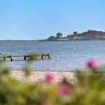 Lake shore with wooden pier and sandy beach. Hills with trees in the background.