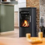 Black wood-burning stove with fire against stone wall.