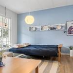 A room with blue wall, futon bed, table, and window.